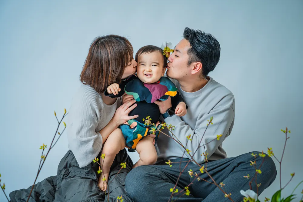 ベージュの服でそろえた両親が子どもの頬にキスをする家族写真（白リンクコーデ例）