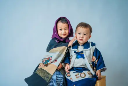 紫のスカーフをまとった着物の子どもと青い羽織袴の幼児が寄り添って座る七五三の兄弟ショット