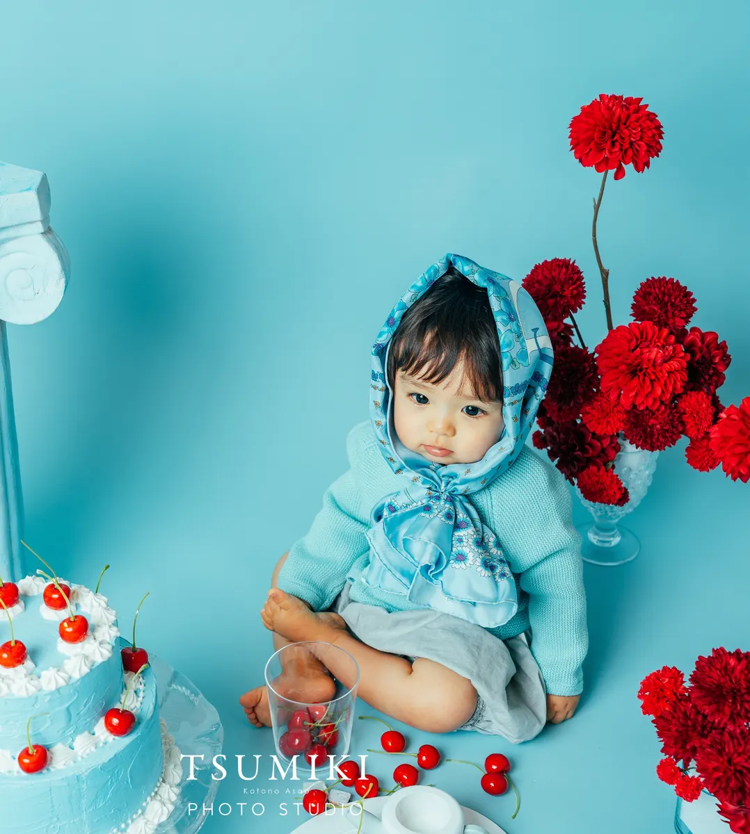 水色の背景で赤い花とともに写る赤ちゃん(Cherry シーン)