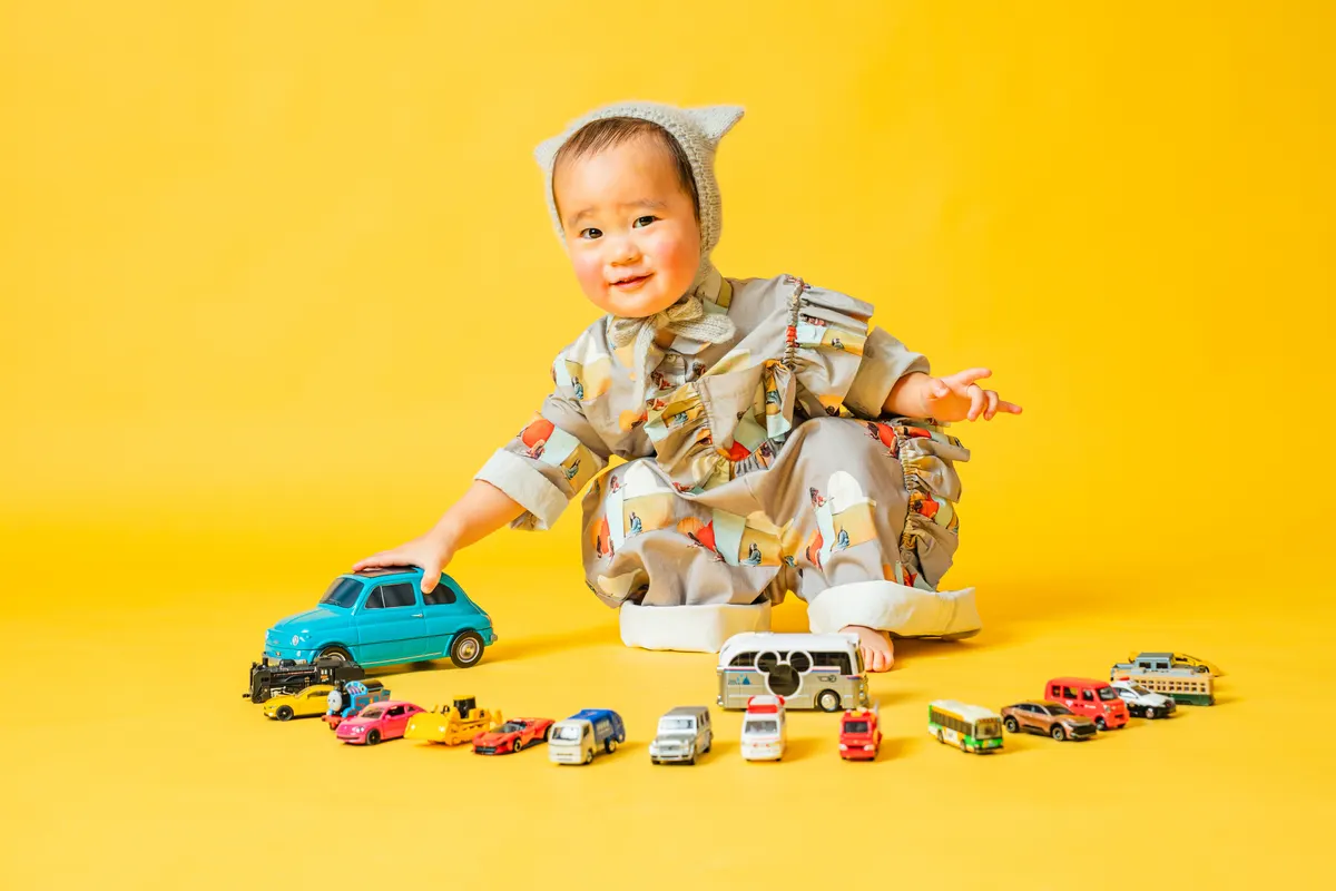 黄色い背景でミニカーを並べて遊ぶ子ども(Classic Portrait シーン)