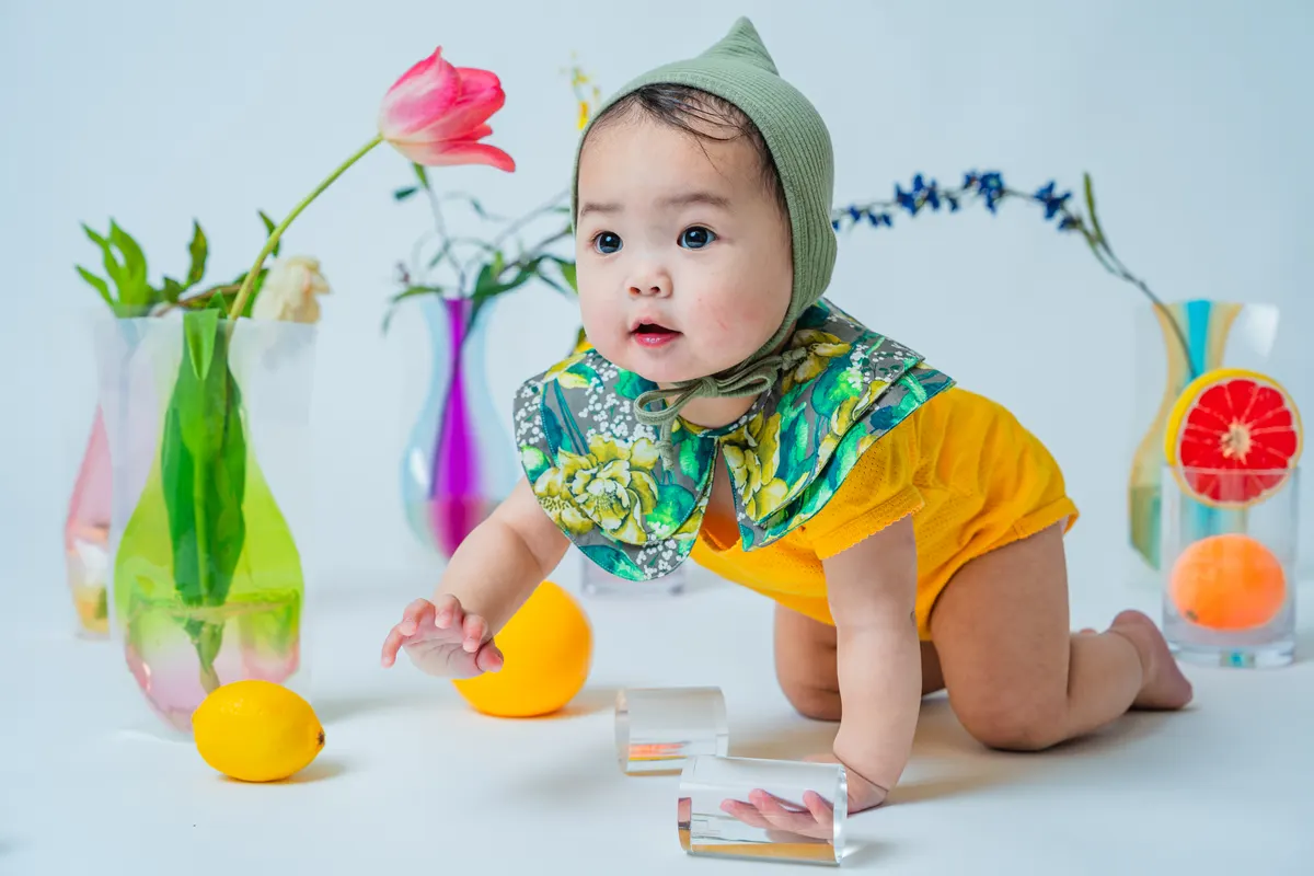 柑橘の果物と花に囲まれてハイハイする黄色い衣装の赤ちゃん(Fruit シーン)