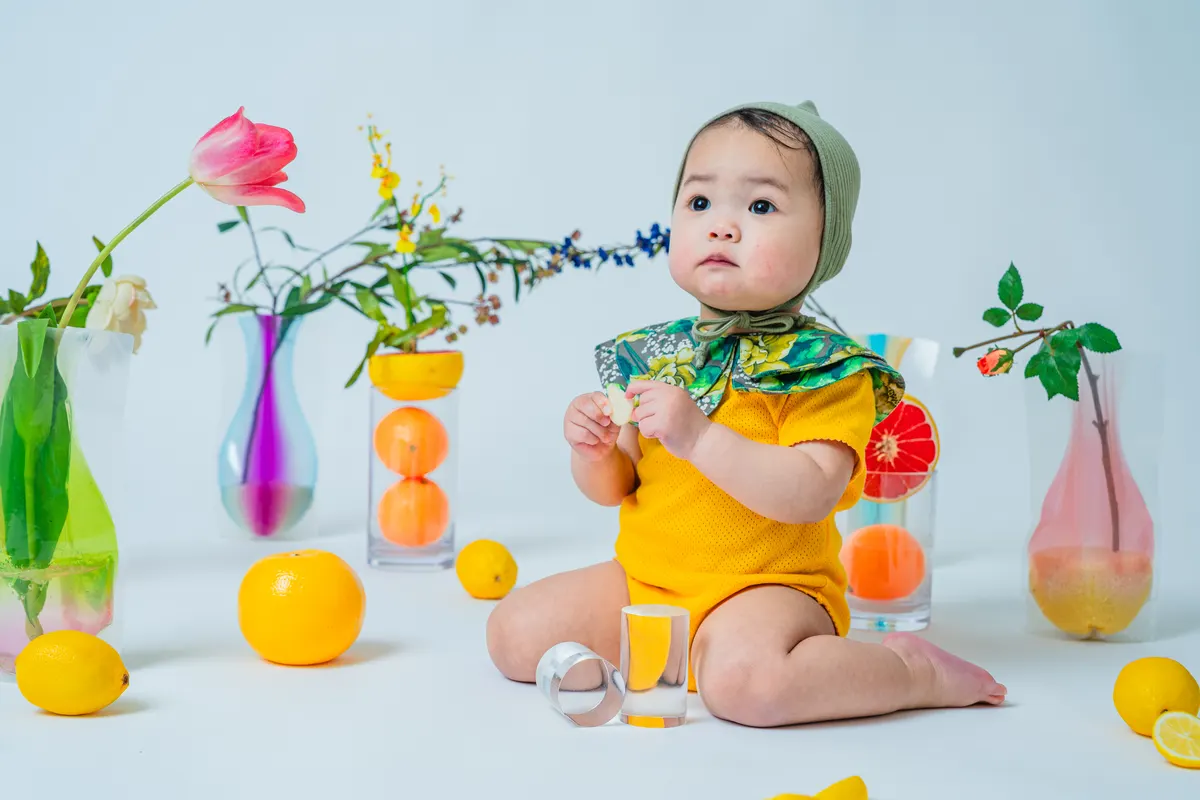 透明感のある果物と花に囲まれた黄色い衣装の赤ちゃん(Fruit シーン)