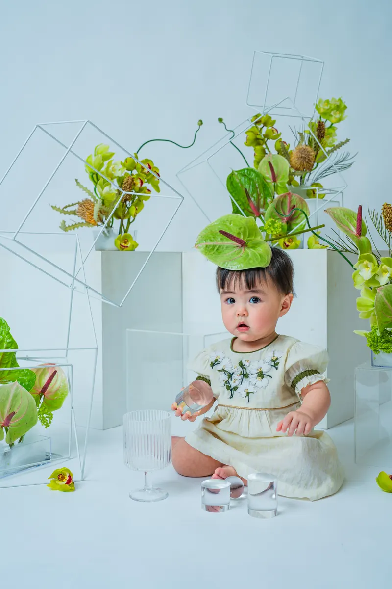頭に緑の葉をのせてグラスで遊ぶ赤ちゃん(Garden シーン)