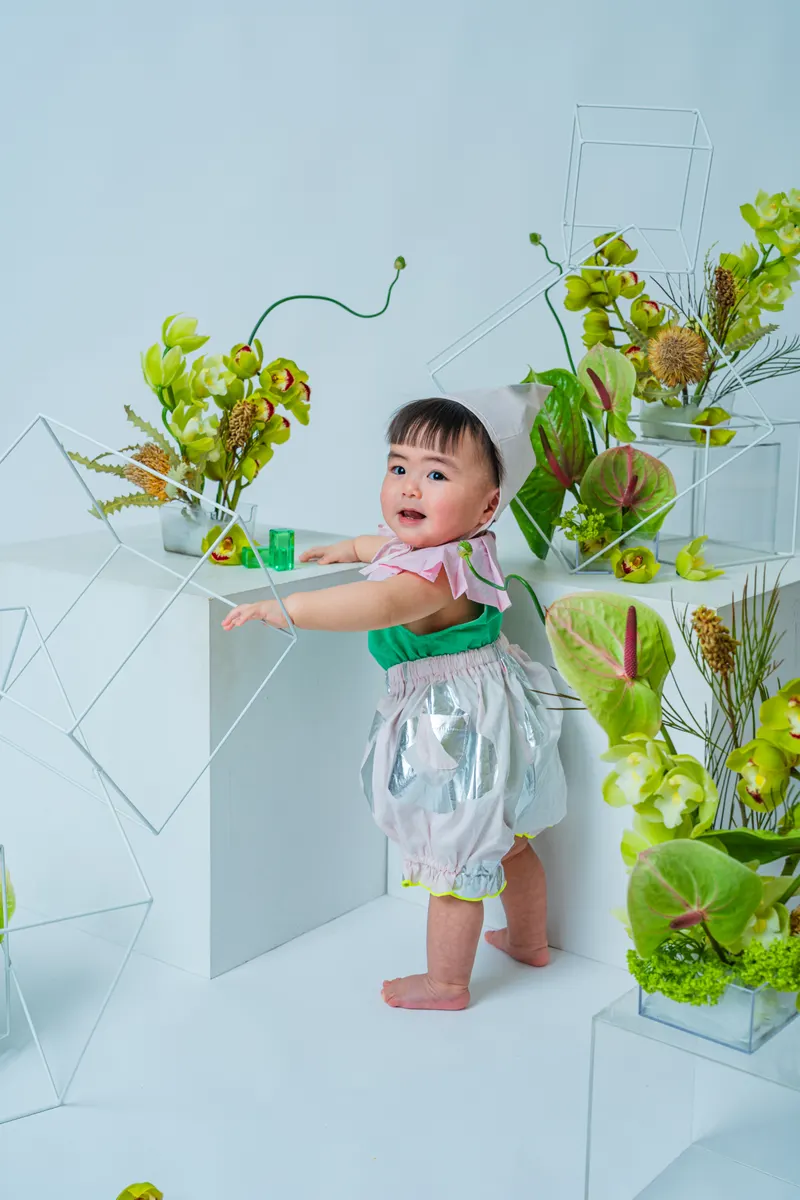 緑の花のセットに手をかけて笑う赤ちゃん(Garden シーン)