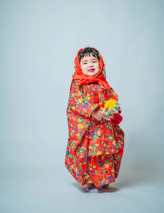 朱赤地に扇や蝶を重ねた総柄の着物「錦」を着た女の子