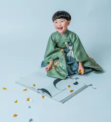 折り紙の本の前で笑う緑の着物姿の七五三の女の子（Orizuru シーン）