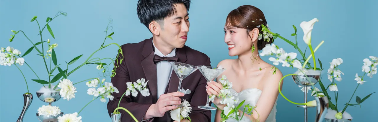白い装花のテーブルでグラスを傾けて乾杯する新郎新婦（Table シーン）